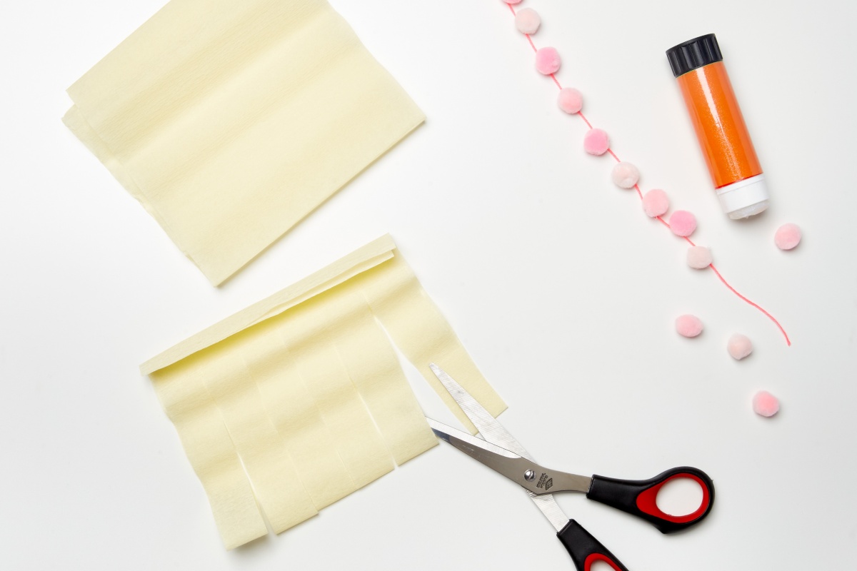 Schere, Klebestift, gelbes Krepppapier und rosa Pompons zum Basteln für die Schultüte