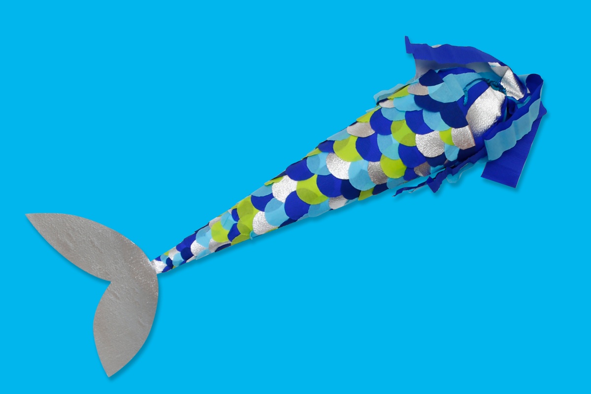 Selbst gebastelte Schultüte im Meerjungfrauen-Design mit blauen, grünen, silberfarbenen Schuppen und Flosse vor blauem Hintergrund.