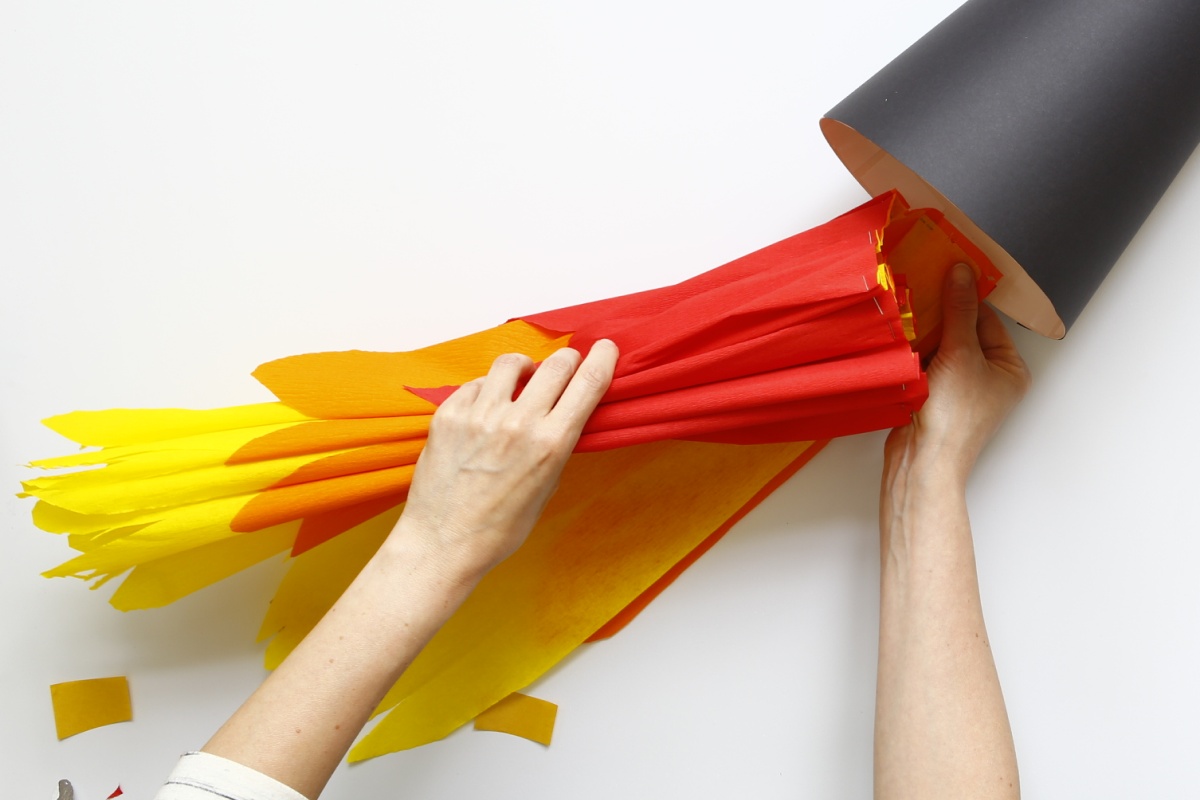 Hände befestigen gelbe, orange und rote Krepppapierstreifen an schwarzer Schultüte.