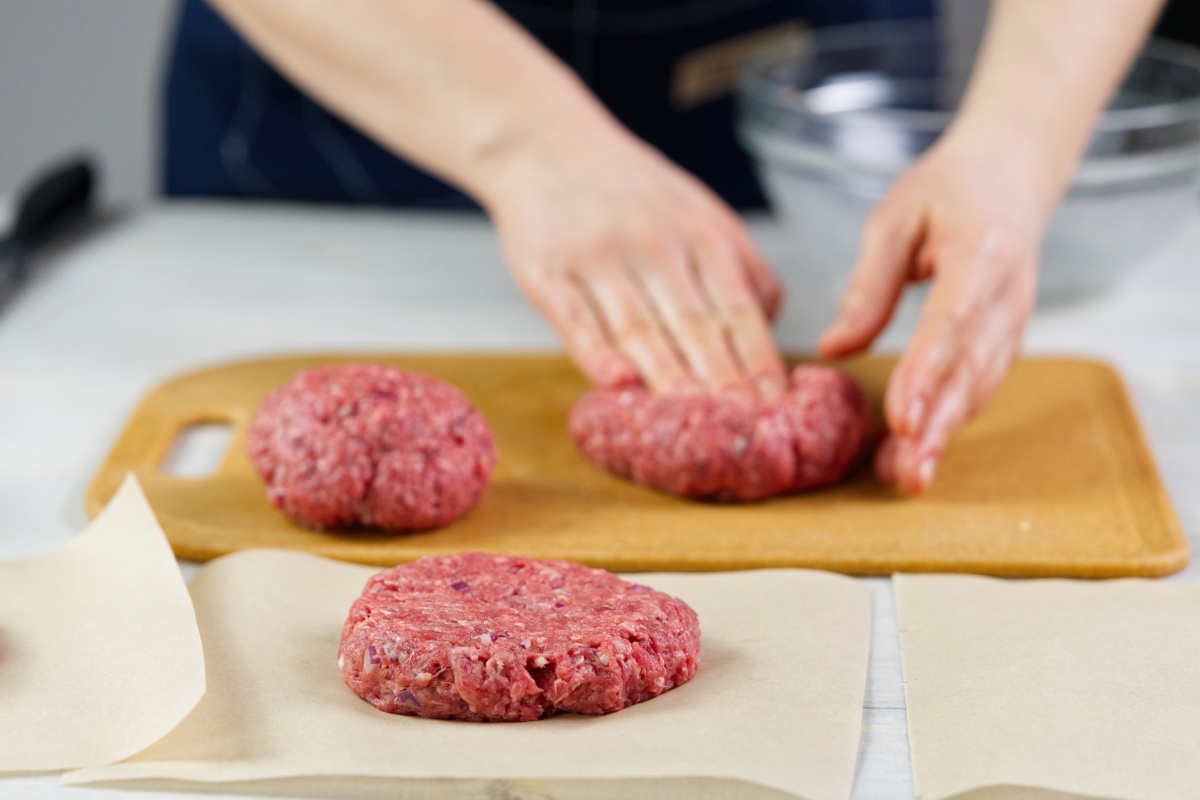 Eine Person formt mit den Händen aus Hackfleisch Burger-Patties.