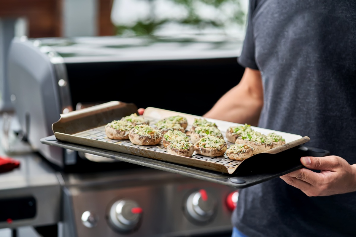 Eine Person trägt gefüllte Champignons zum Grill.
