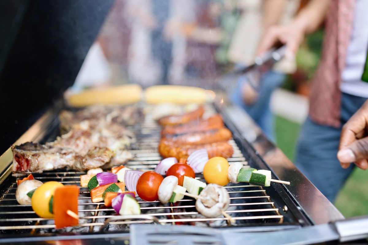 Vegetarische Grillspieße, Fleisch, Würstchen und Maiskolben auf einem Grill.