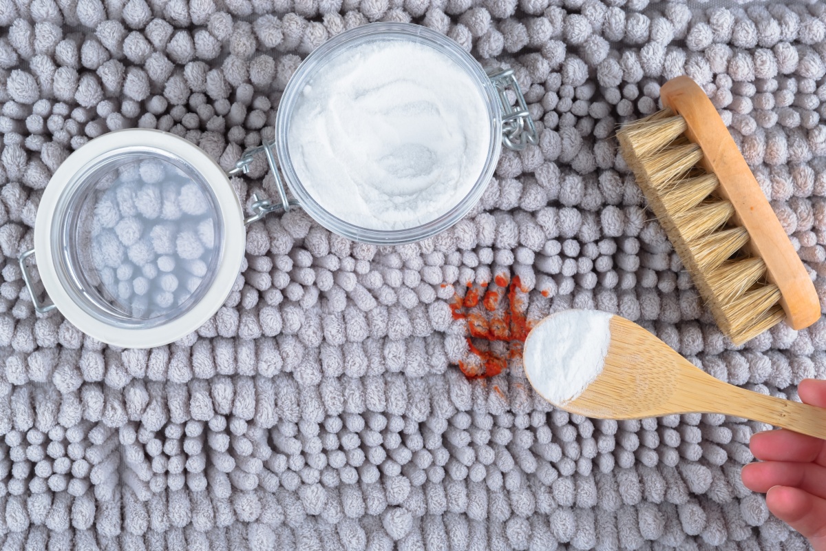 Person reinigt einen roten Teppichfleck mit Backpulver und Bürste.