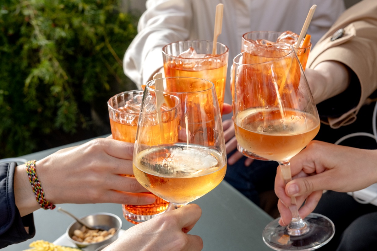 Mehrere Personen stoßen mit Aperol Spritz und Weißwein an bei einer Gartenparty im Freien an.