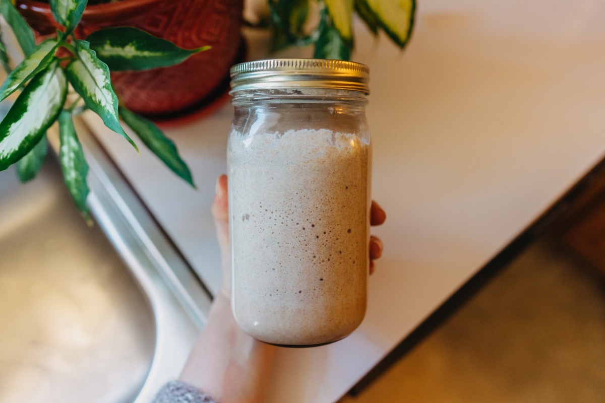 Eine Person hält ein Glas mit aktivem Sauerteig in der Hand.