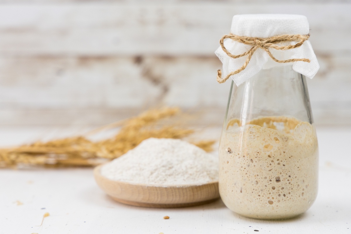 Einmachglas mit aktivem Sauerteig neben einer Schale Mehl.