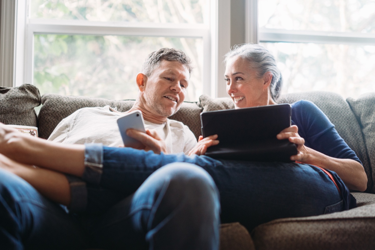 Ein Paar sitzt entspannt auf dem Sofa und nutzt gemeinsam Smartphone und Tablet.