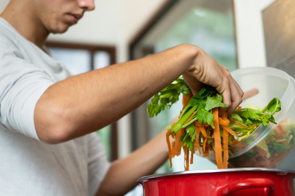 Person gibt frischen Gemüseabfall in einen Topf für den Kompost.