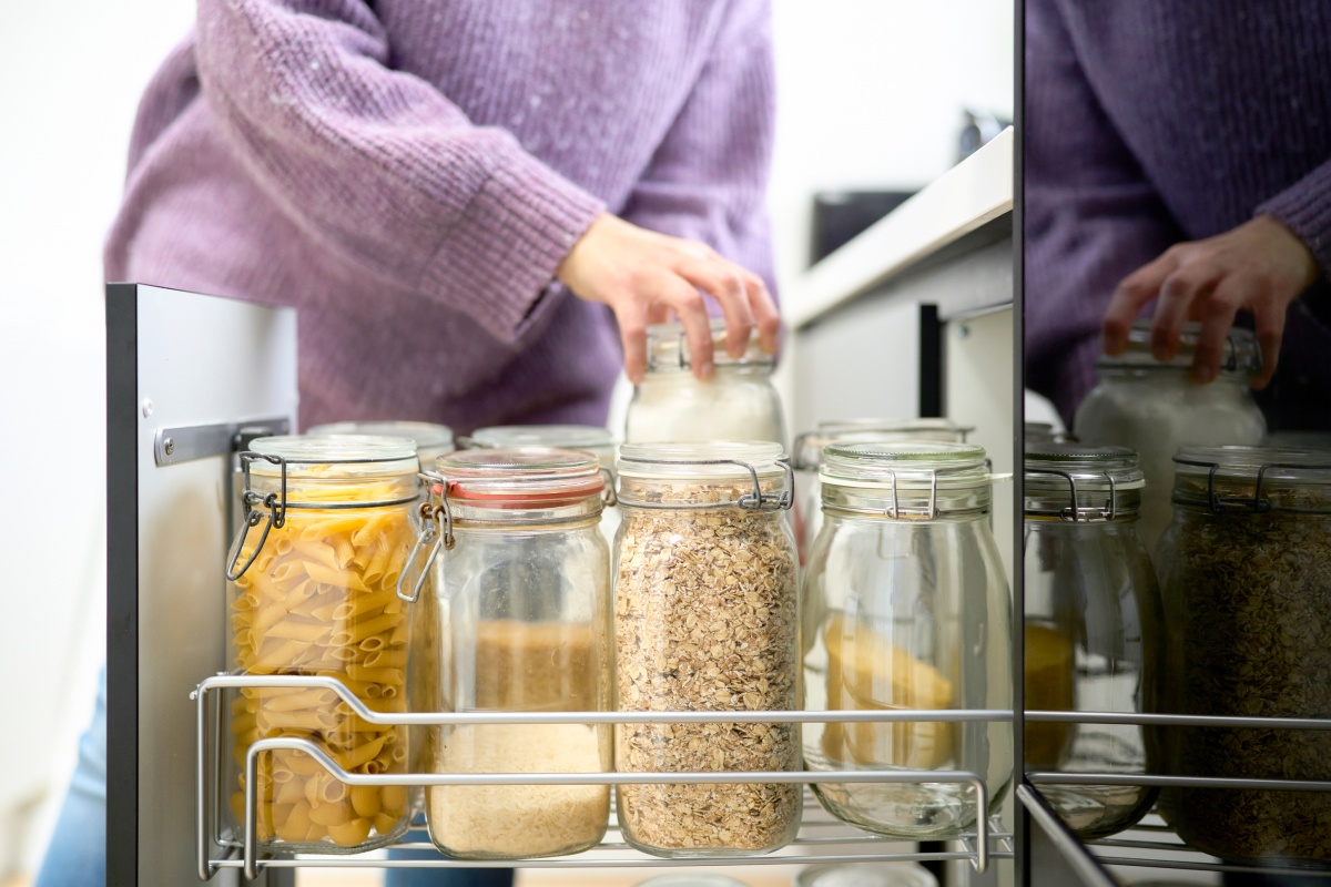 Person ordnet Vorratsgläser mit Nudeln und Getreide im Küchenschrank.