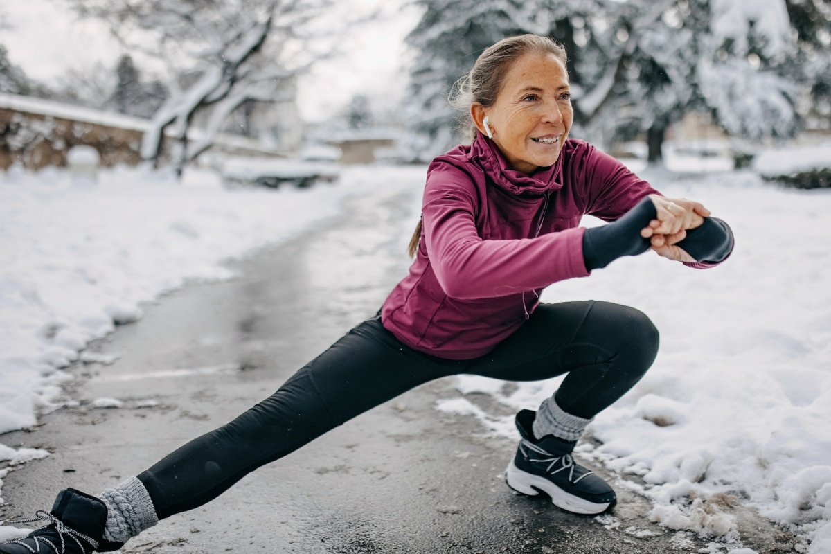 Frau macht seitliche Dehnübung in der Hocke auf einem verschneiten Weg.