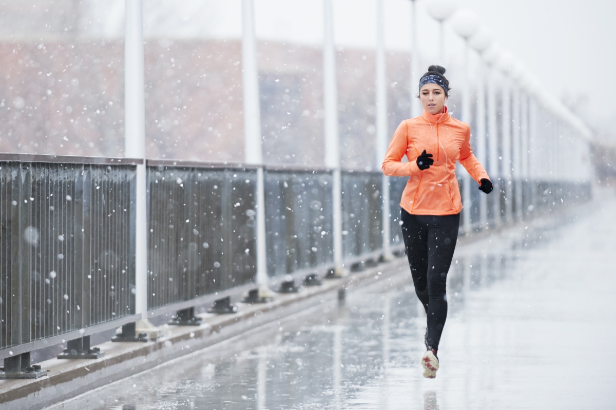 Frau joggt bei Schneefall auf einer eisglatten Brücke.