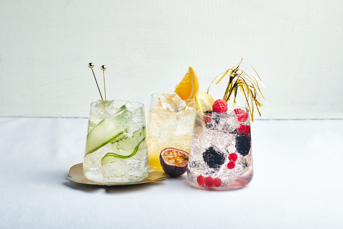 Drei verschiedene Cocktails in Gläsern, dekoriert mit Gurke, Passionsfrucht, Beeren und Zitrusfrüchten.