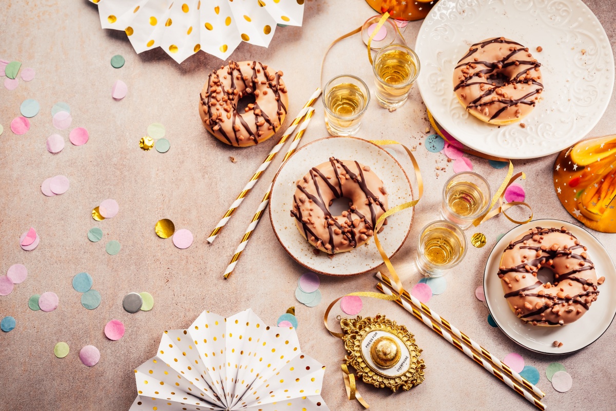 Festliche gedeckter Tisch mit Donuts, Konfetti, goldenen Trinkhalmen und kleinen Gläsern.