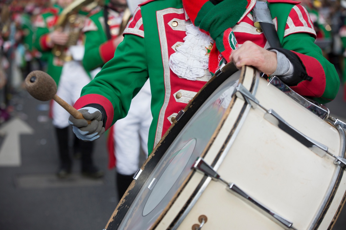 Musiker in grün-roter Uniform spielt große Trommel während eines Karnevalsumzugs.