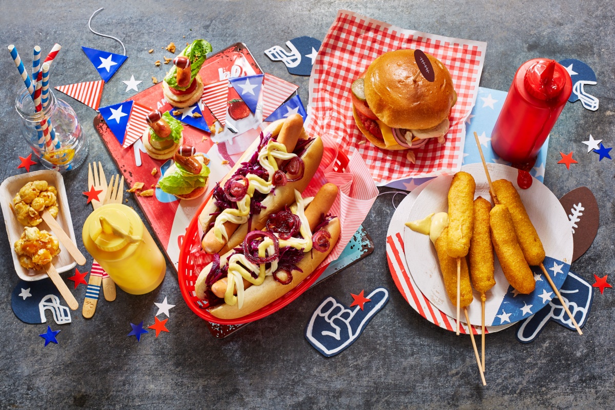 Snacks wie Burger, Corndogs, Hot-Dogs auf bunten Tabletts, dekoriert im amerikanischen Stil.
