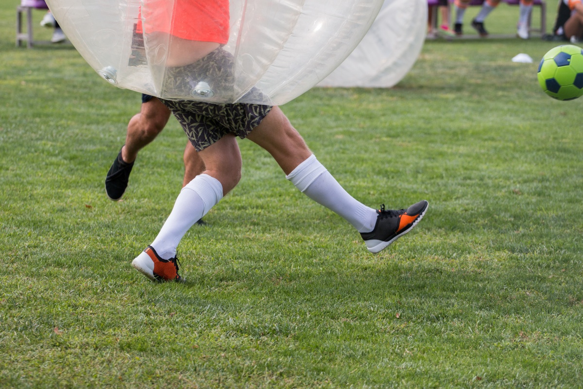 Zwei Personen spielen Bubble-Soccer auf einer Grünfläche. 