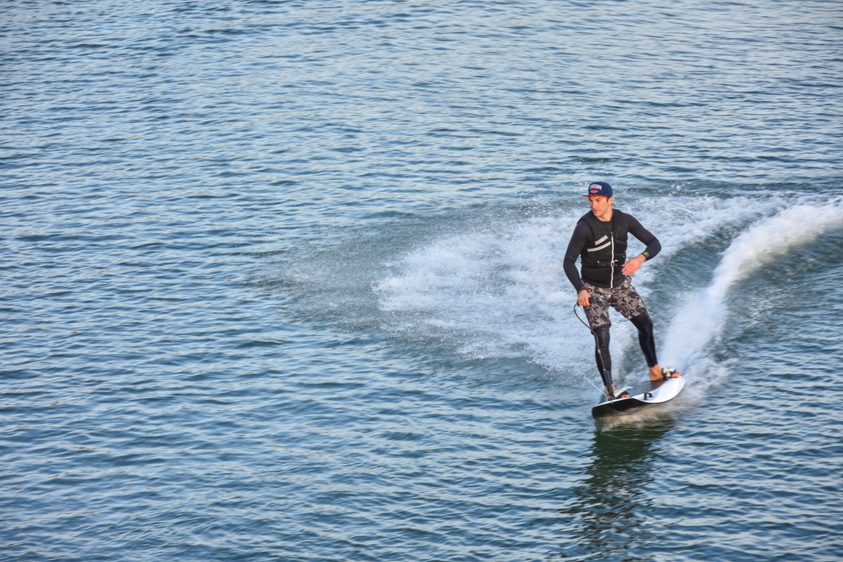 Mann in Neoprenanzug steht auf Surfbrett nach dem er Jetsurfing gemacht hat.