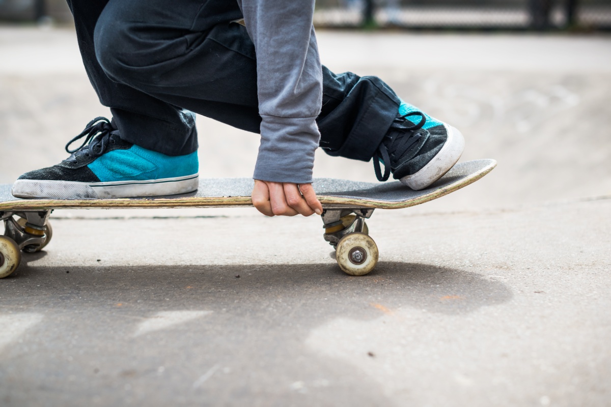Person mit sportplichen Sneakern auf einem Skateboard in der Hocke.