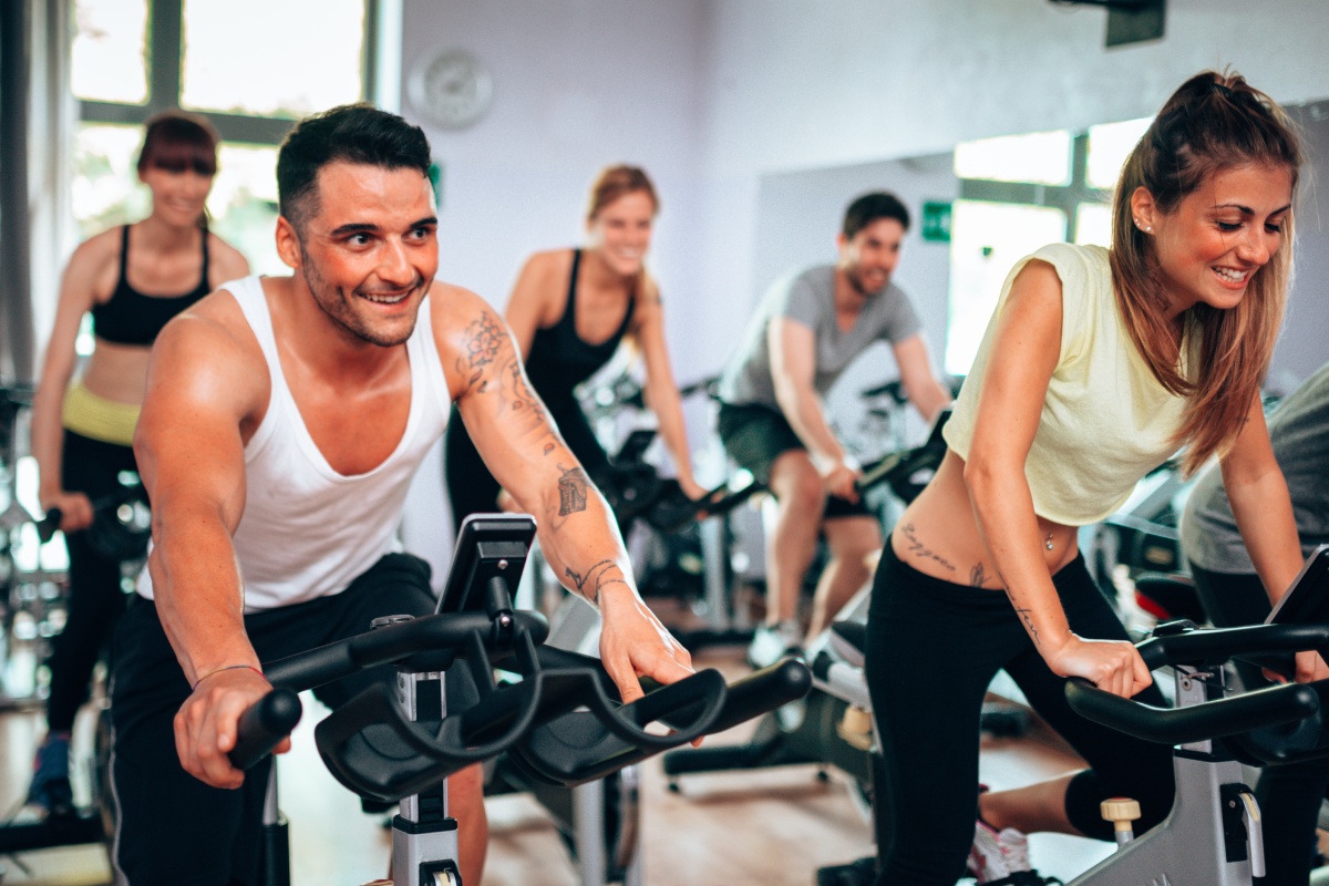 Mehrere Personen im Fitnessstudio auf Hometrainern beim Spinning.
