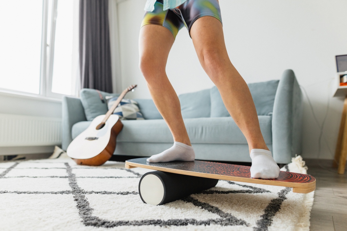 Person mit weißen Socken und Kurzer Hose auf einem Balanceboard im Wohnzimmer