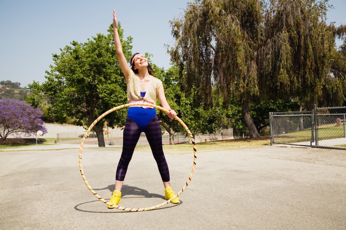 Frau in Legging und Body mit einem Hulahoop-Reifen im Freien.