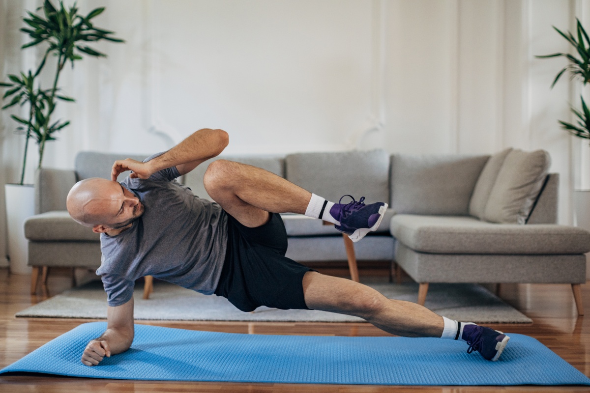 Mann macht Side-Crunches auf einer blauen Fitnessmatte im Wohnzimmer zu Hause.