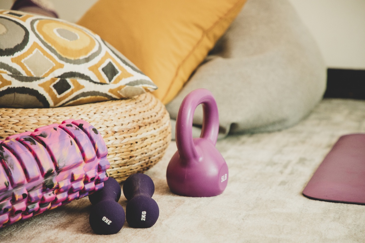 Auf dem Boden liegen zwischen Sitzkissen und Yogamatte eine Kettlebell, Kurzhanteln und Schaumstoffrolle.