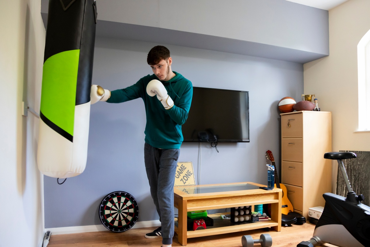 Mann trainiert mit Boxsack im Home Gym umgeben von Fitness-Equipment.
