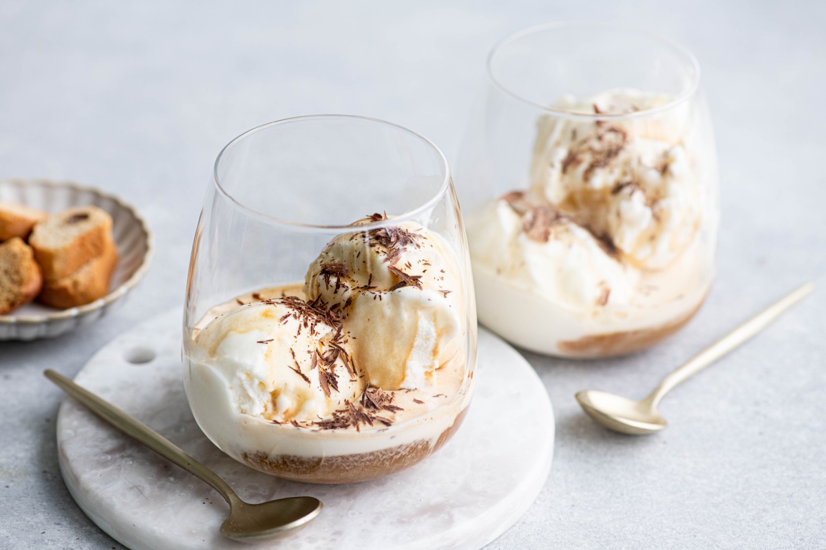 Zwei Gläser Eiskaffee mit Vanilleeis und Espresso, dekoriert mit Schokoraspeln, daneben goldene Löffel.