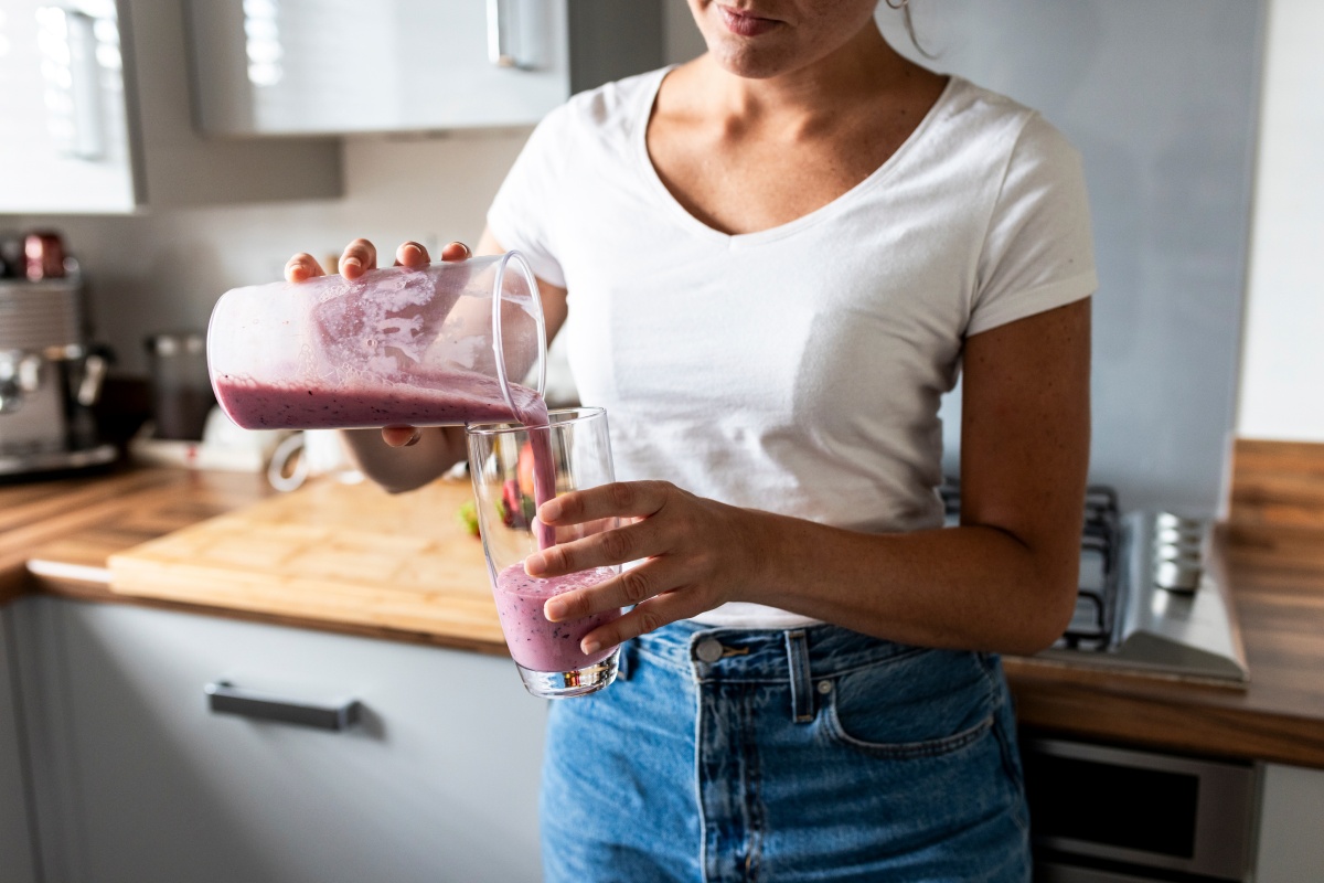 Frau gießt sich einen frischen Beeren-Smoothie aus Mixer ins Glas