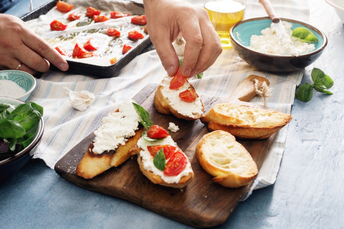 Jemand belegt geröstete Baguettescheiben mit Ricotta und frischen Tomaten.