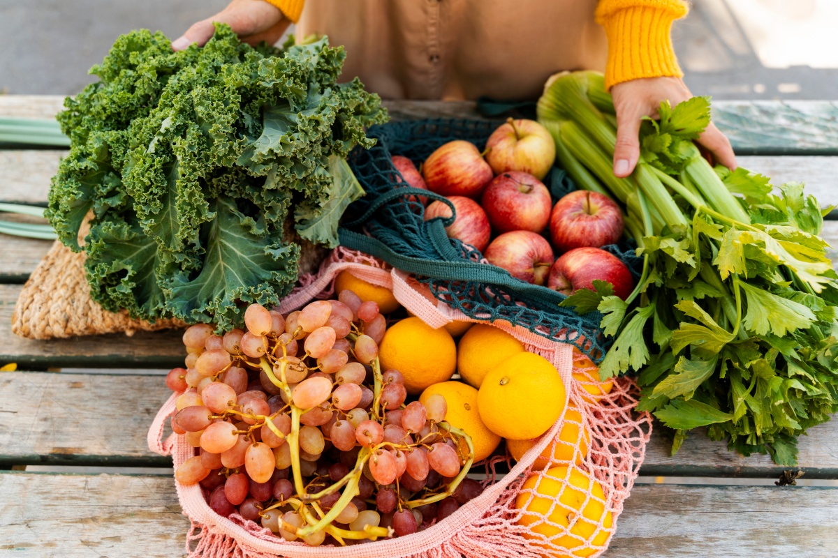 Bunte Auswahl an frischem Gemüse und Obst, darunter Grünkohl, Äpfel, Sellerie, Trauben und Orangen auf einem Holztisch.