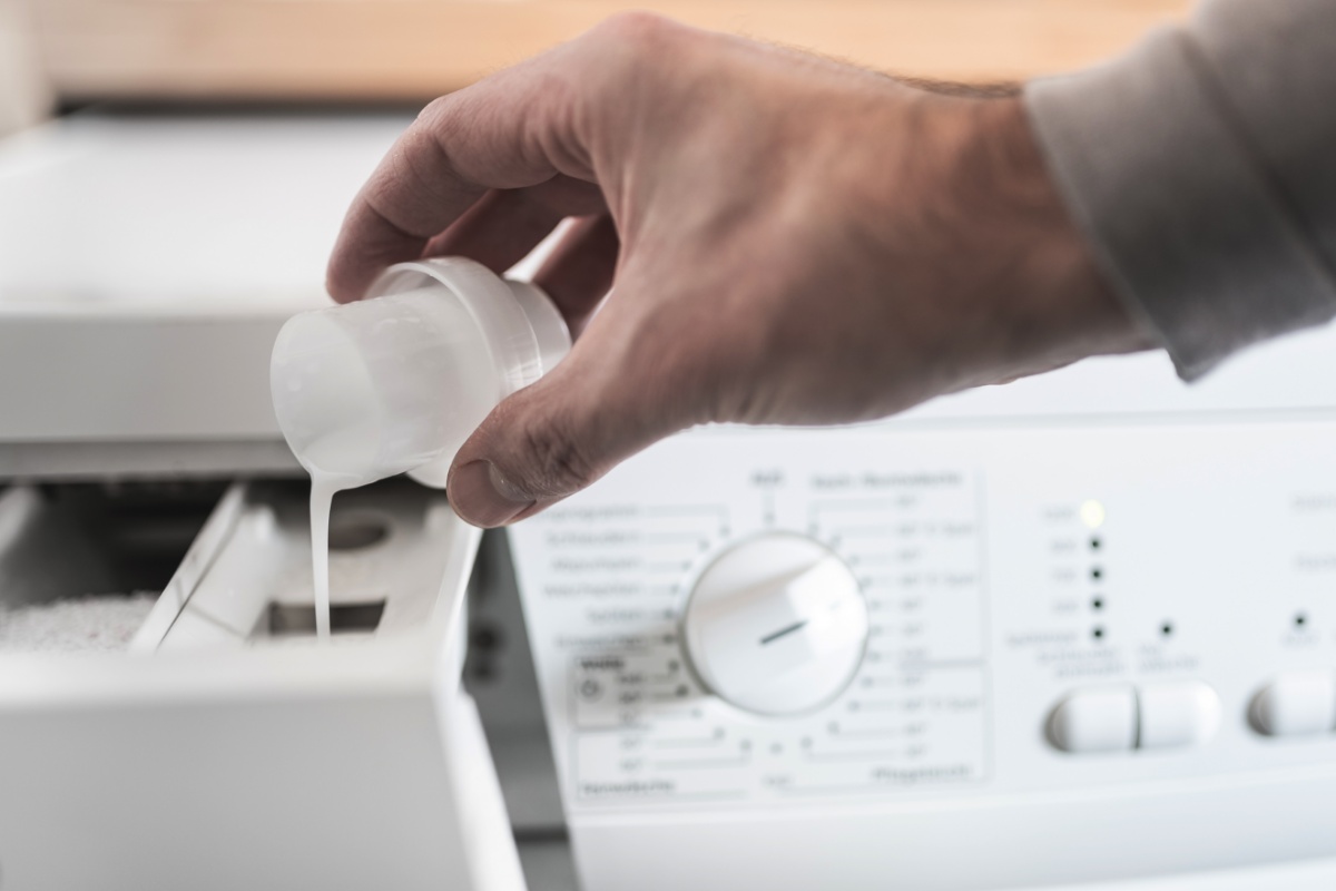 Eine Person dosiert Waschmittel in die Waschmaschine.