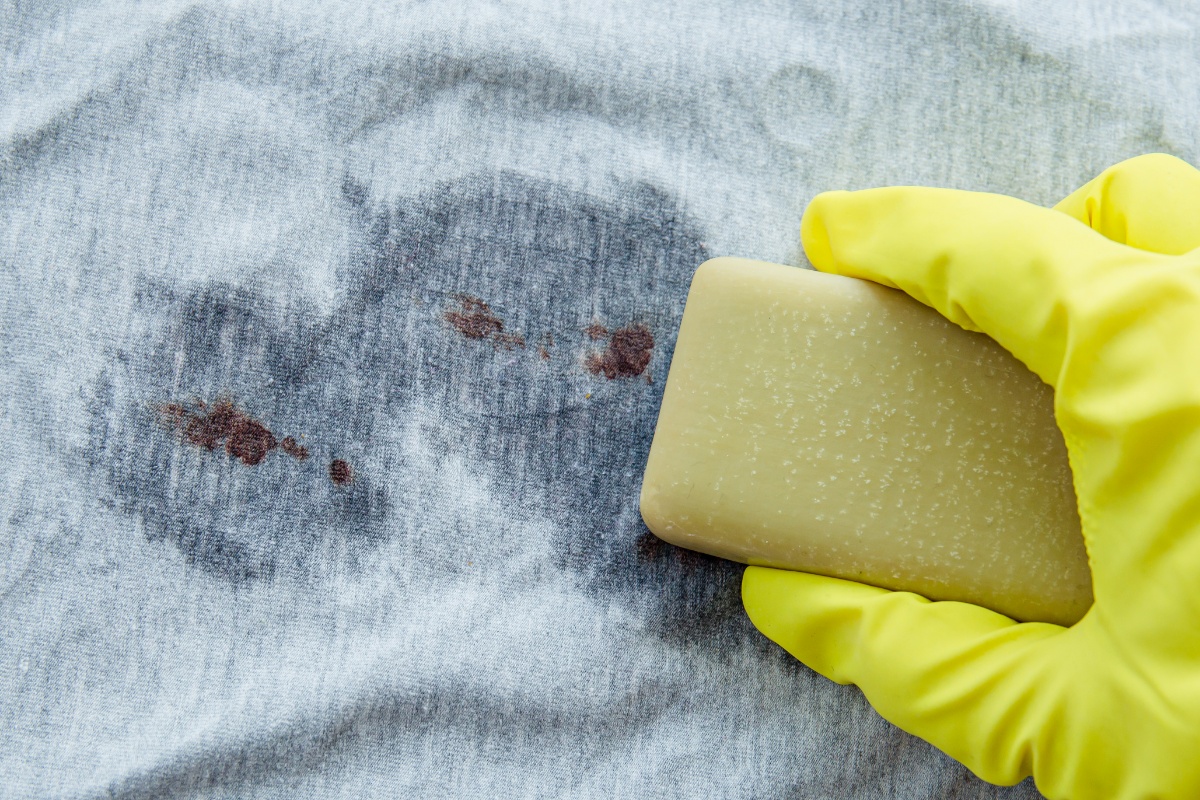 Eine Hand behandelt Flecken auf einem Shirt mit Gallseife vor.