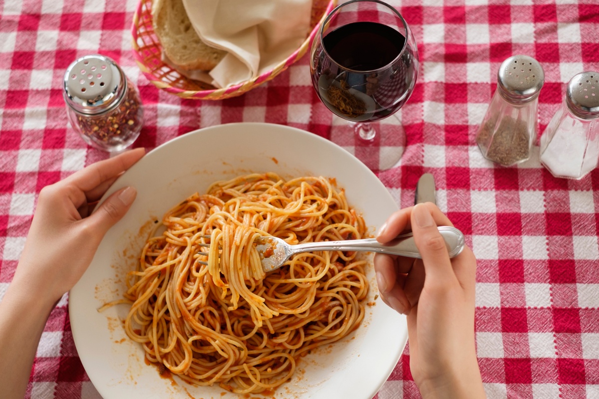 Eine Person isst Spaghetti Bolognese, dazu ein Glas Rotwein.