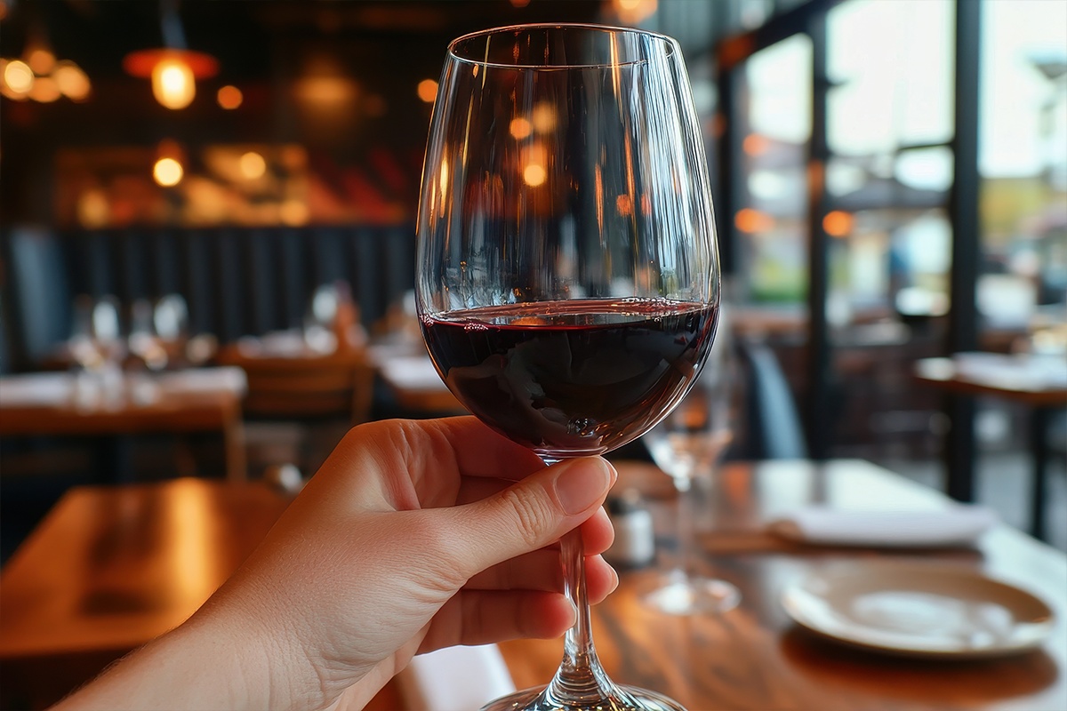 Spätburgunder im Weinglas wird hochgehalten von einer Hand im Restaurant.