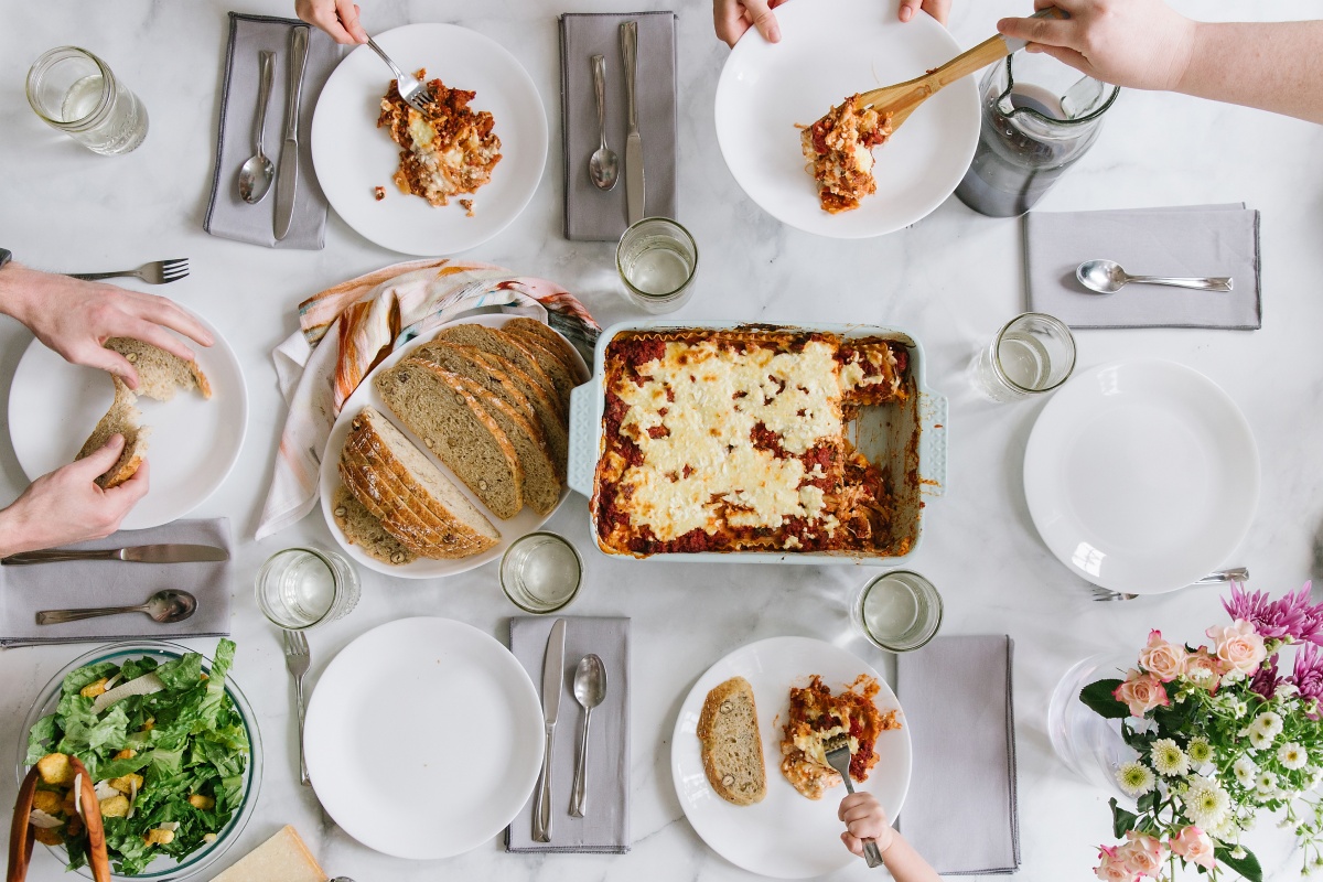 Gedeckter Tisch mit Lasagne, frischem Brot, Salat und Getränken für gemeinsames Essen.