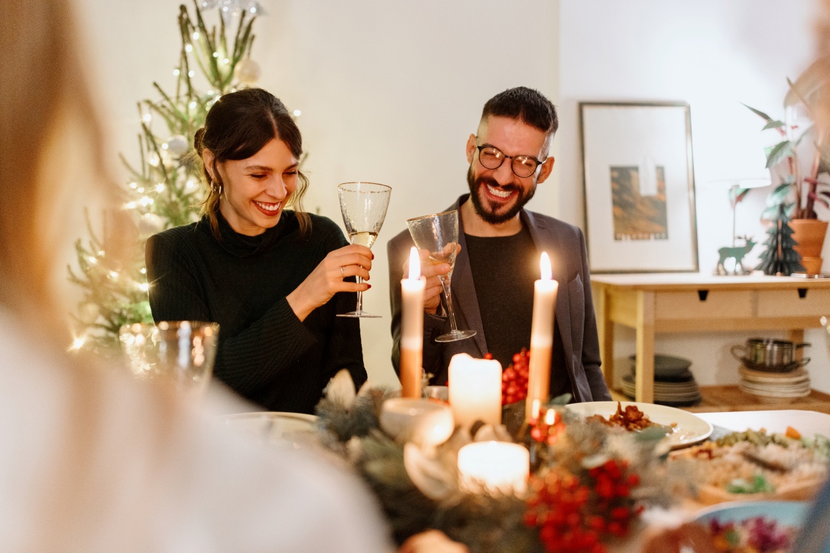 Lächelnde Gäste an einem festlich gedeckten Tisch stoßen mit Sektgläsern an.