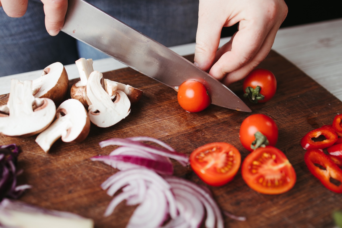 Person schneidet frisches Gemüse, darunter Tomaten, Pilze und Zwiebeln.
