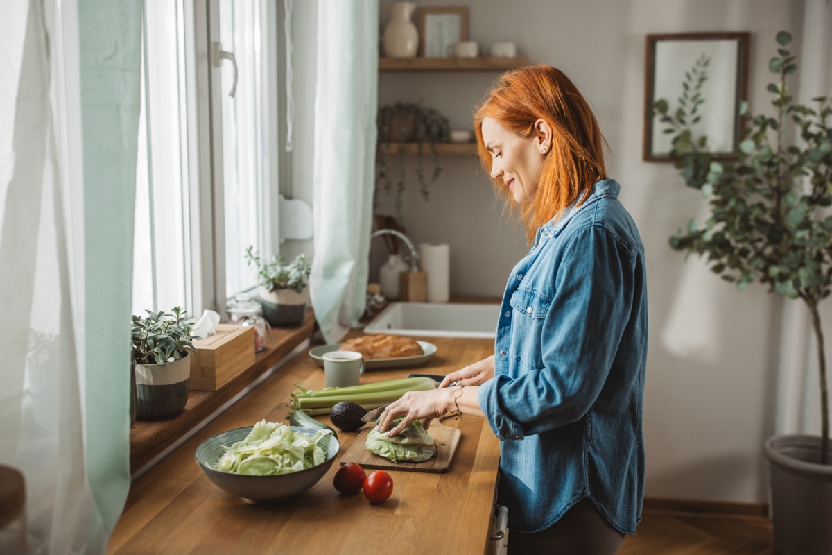 Frau schneidet frischen Salat in einer hellen, gemütlichen Küche.