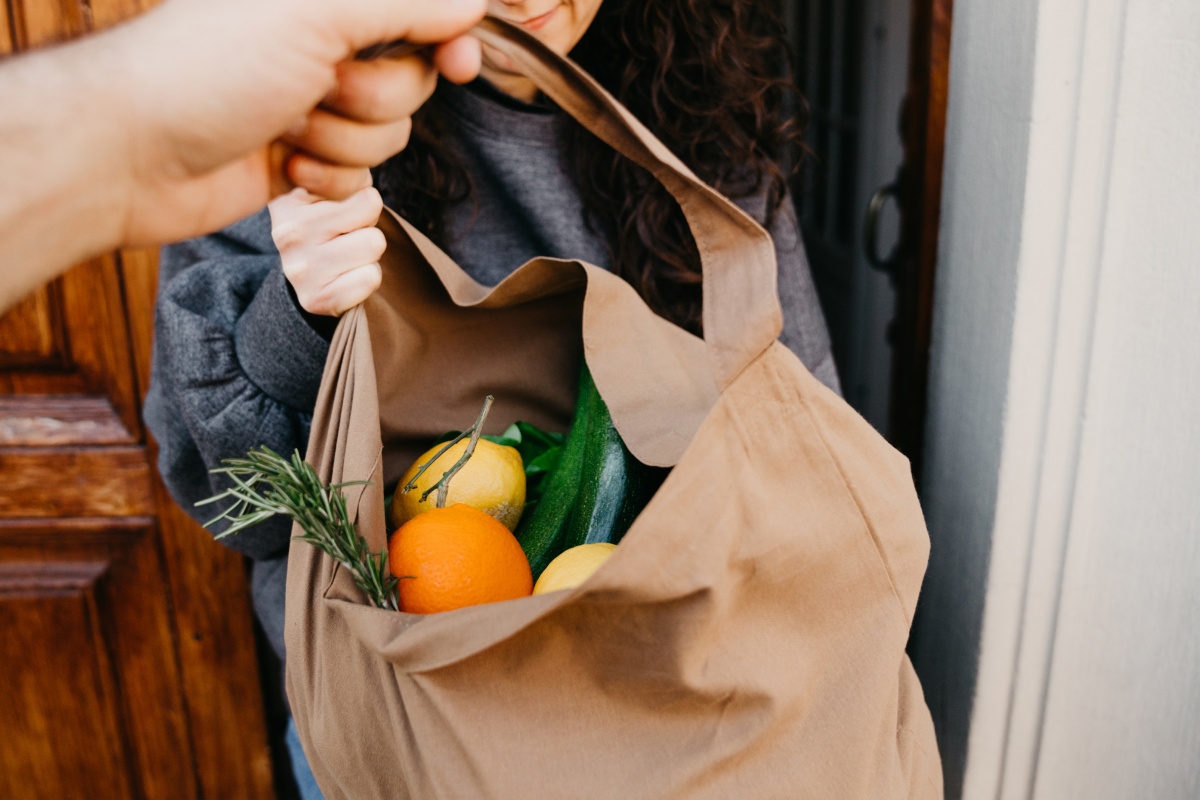 Person überreicht Stofftasche mit frischem Obst und Gemüse.