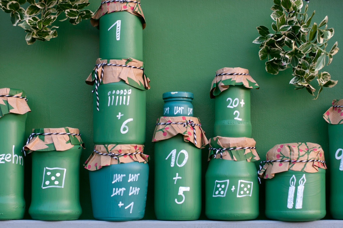 Adventskalender aus grün bemalten Gläsern mit Zahlenrätsel als Nummerierungen.