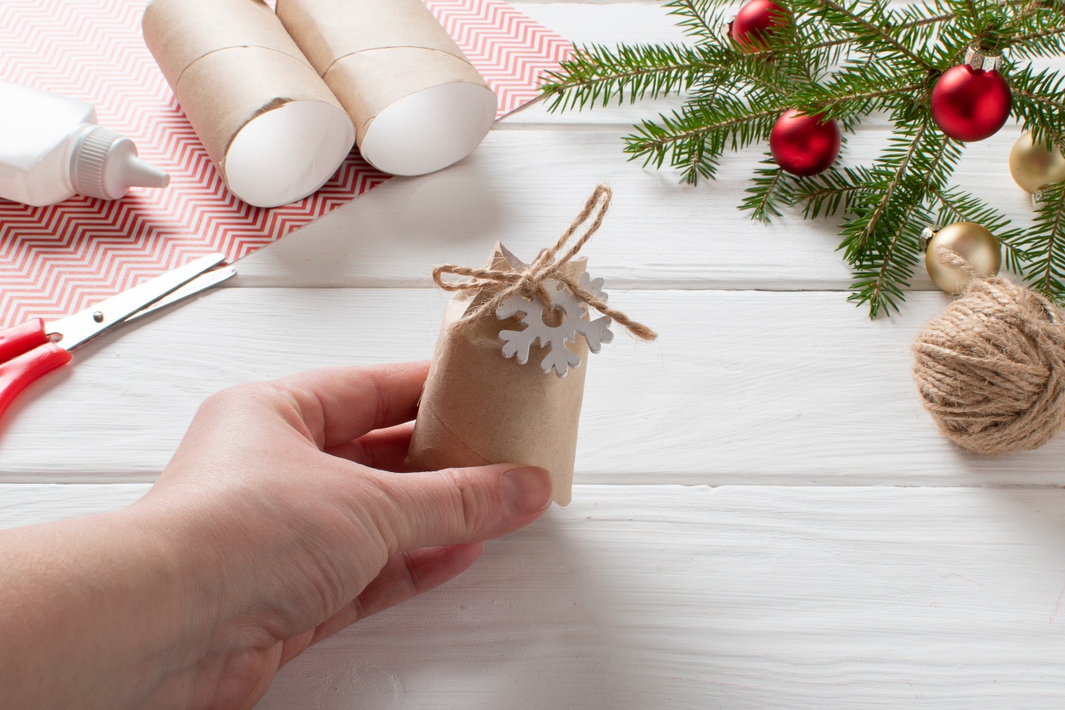 Jemand hält eine aus einer Klopierrolle gebastelte Tüte eines Adventskalenders, im Hintergrund Bastelmateialien und Weihnachtsdekoration.