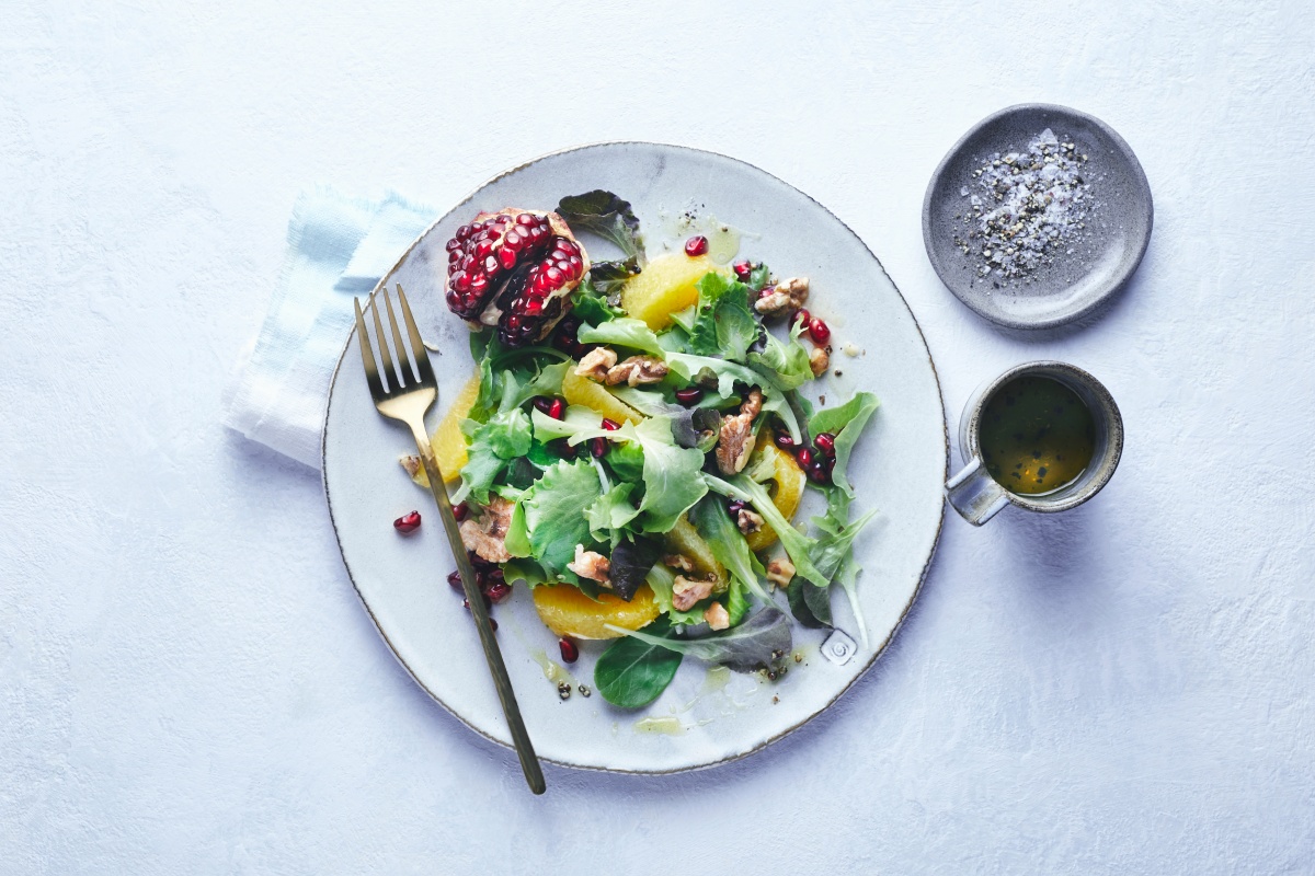 Frischer Salat mit Granatapfelkernen, Walnüssen und Orangenscheiben auf Teller.