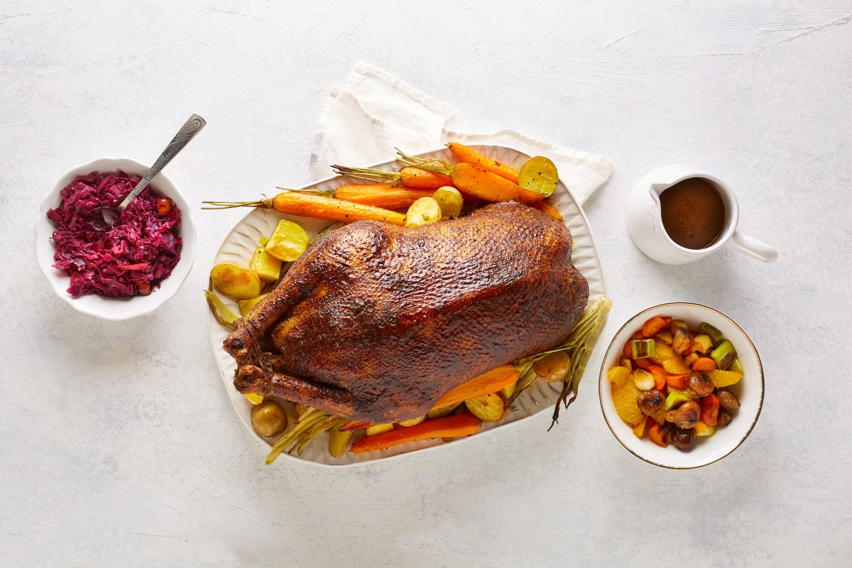 Gebratene Gans mit Kartoffeln, Möhren und Beilagen wie Rotkohl und Soße auf weißem Tisch.