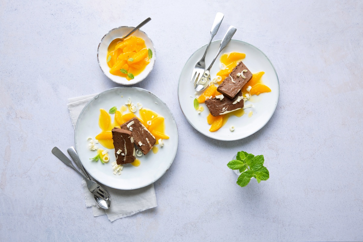 Schokoladen-Parfait mit Orangenfilets und weißen Schokospänen auf weißem Teller.