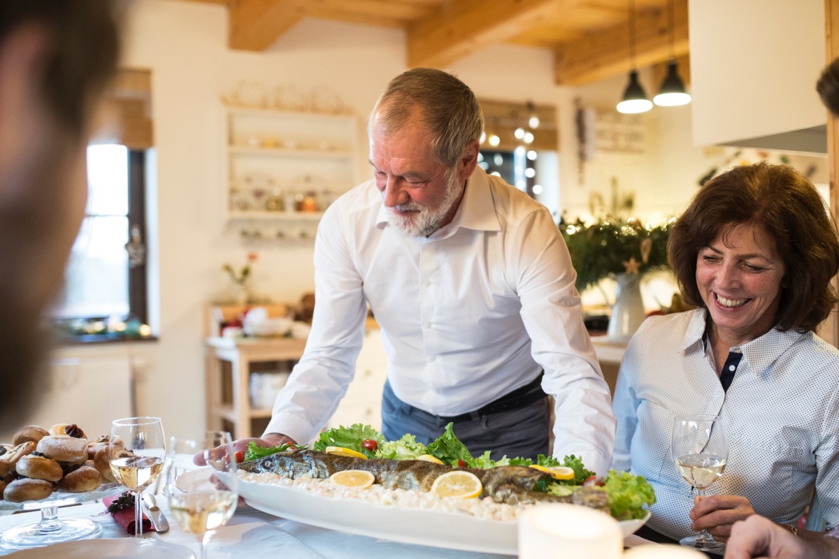 Älterer Mann serviert festliche Fischplatte mit Zitrone zum Weihnachtsessen.