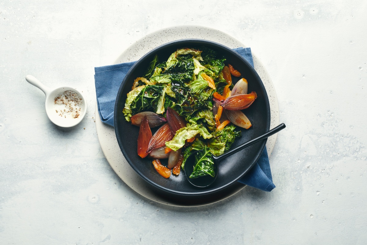 Gebratener Wirsing mit Schalotten und Gewürzen auf schwarzem Teller.