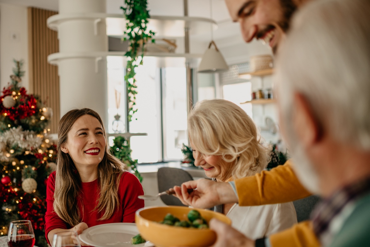 Familie sitzt lächelnd am festlich dekorierten Tisch beim Weihnachtsessen.