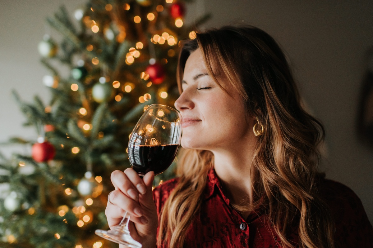 Frau genießt Rotwein vor festlich beleuchtetem Weihnachtsbaum.